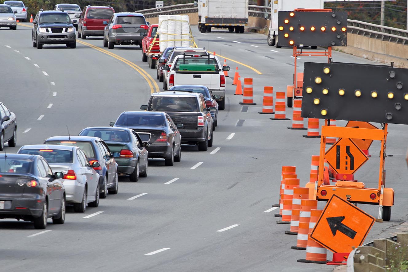 Standard road signs, digital flashing arrows  and traffic cones direct all traffic into the left lane on a road construction site.